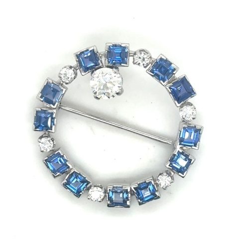 Platinum old European cut diamond and square-cut blue sapphire circle brooch, approx. 0.83 ct OEC featured diamond at crown, 0.54 CTW OEC accent diamonds, square sapphires in alternating collet settings, straight pin bar, Art Deco